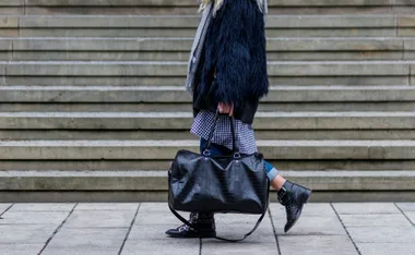 Person walking with a black leather weekender bag on stone steps.