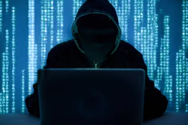 A hooded person at a laptop with a digital code background.