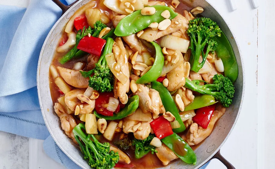 Sweet and sour chicken with vegetables and peanuts in a pan.