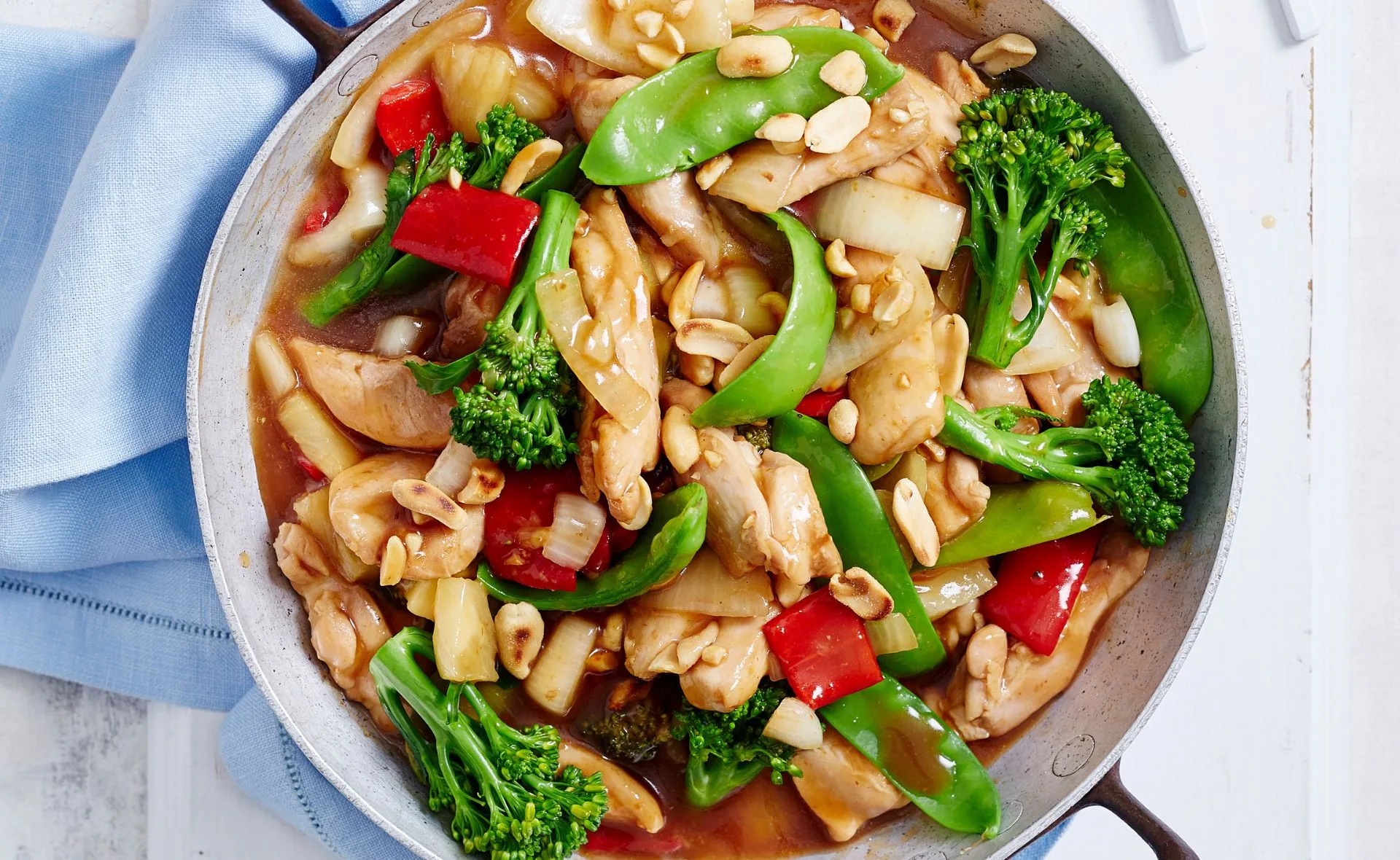 Sweet and sour chicken with vegetables and peanuts in a pan.
