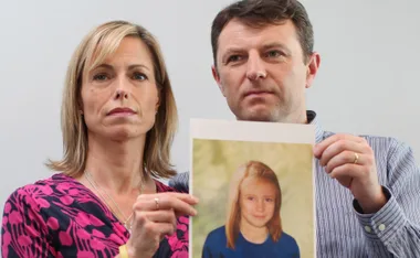 A man and woman hold a photo of a young girl with long blonde hair wearing a blue shirt.