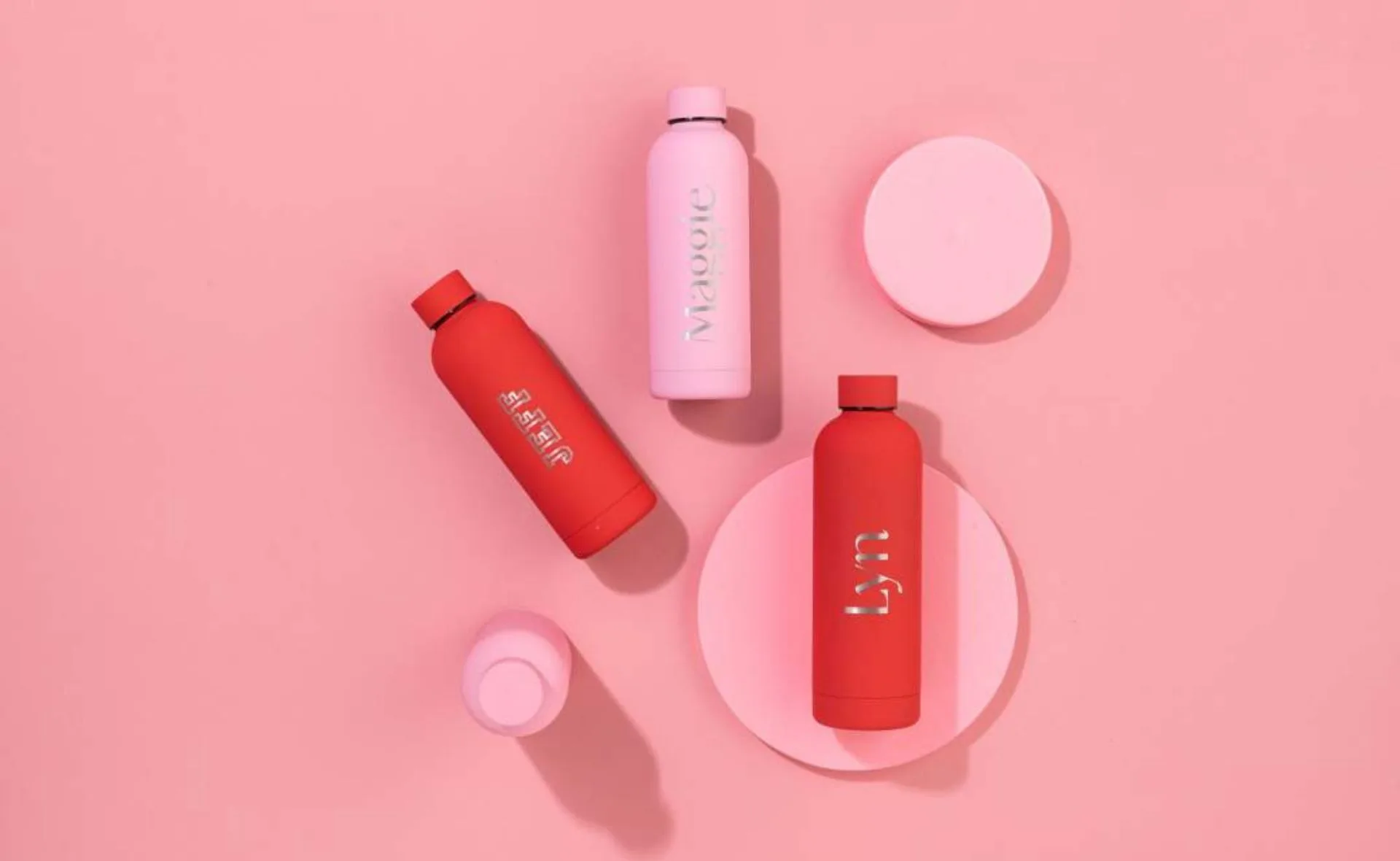 Red and pink personalized bottles with names on a pink background.