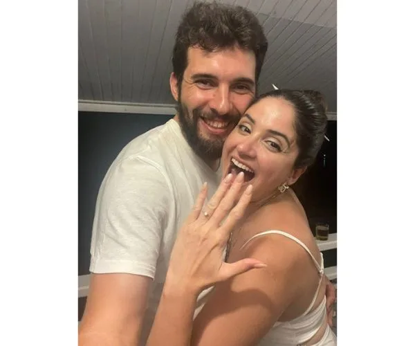 A smiling couple hugs, showing an engagement ring.