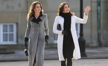 Two well-dressed women walking outdoors, one waving.