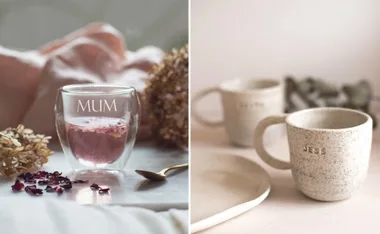 Personalized mugs with "MUM" on a glass cup and "JESS" on a speckled ceramic mug, placed on a table.