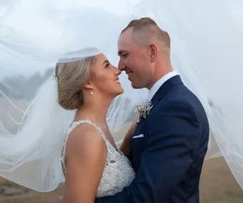 Bride and groom smiling at each other under a flowing veil on their wedding day.