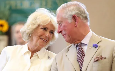 Older couple smiling at each other, wearing formal attire, with blurred background.