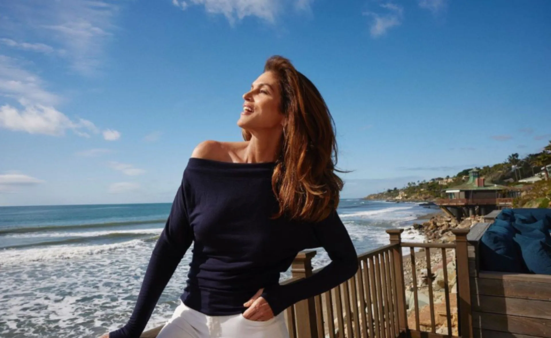 Woman in a dark top enjoying a sunny day on a deck overlooking a scenic ocean view.
