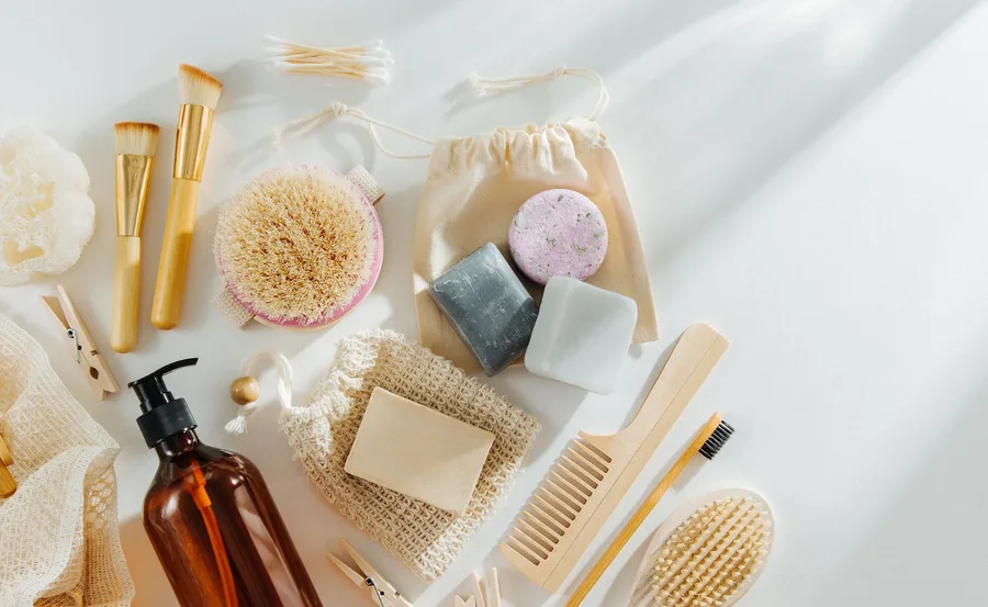 Sustainable bathroom products, including brushes, soaps, reusable bottles, and eco-friendly wooden items on a light background.