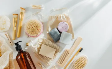 Sustainable bathroom products, including brushes, soaps, reusable bottles, and eco-friendly wooden items on a light background.