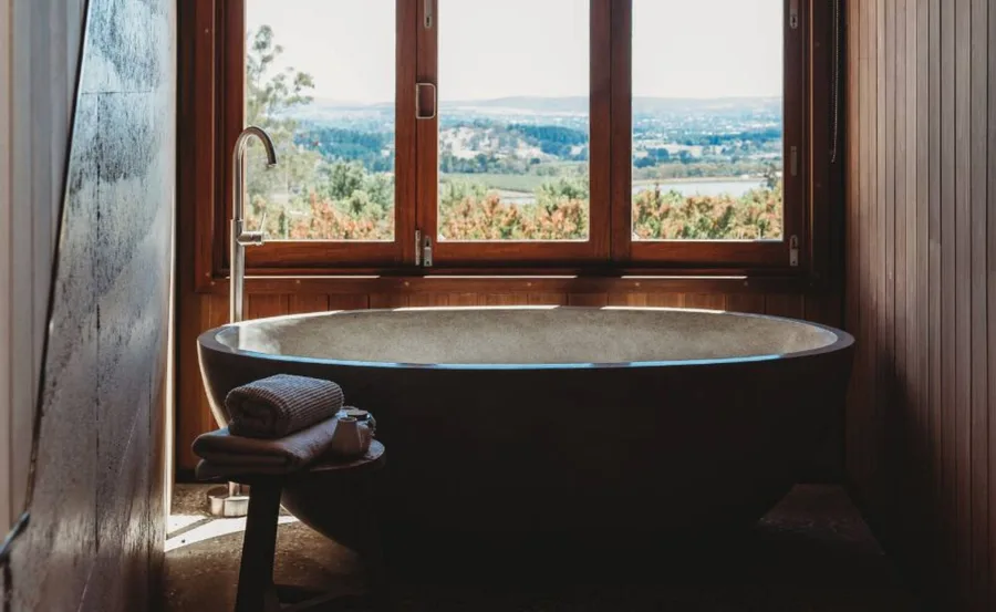 Luxurious bathtub with rolled towels, large window view of lush landscape in upscale accommodation, NSW.