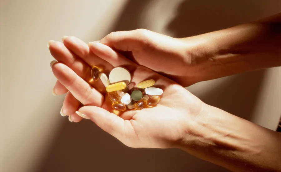 Hands holding various colorful vitamin capsules and tablets.