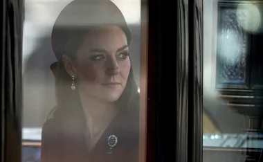 Woman with earrings and hat looking contemplatively out of a window with reflections and soft lighting.
