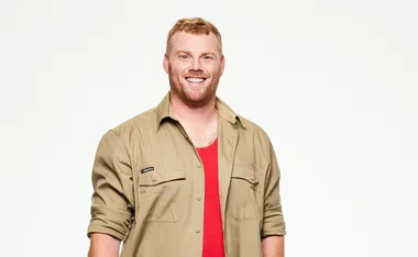 Man smiling in a beige shirt and red tank top against a white background.