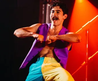 Circus performer in colorful outfit dancing energetically under bright stage lights.