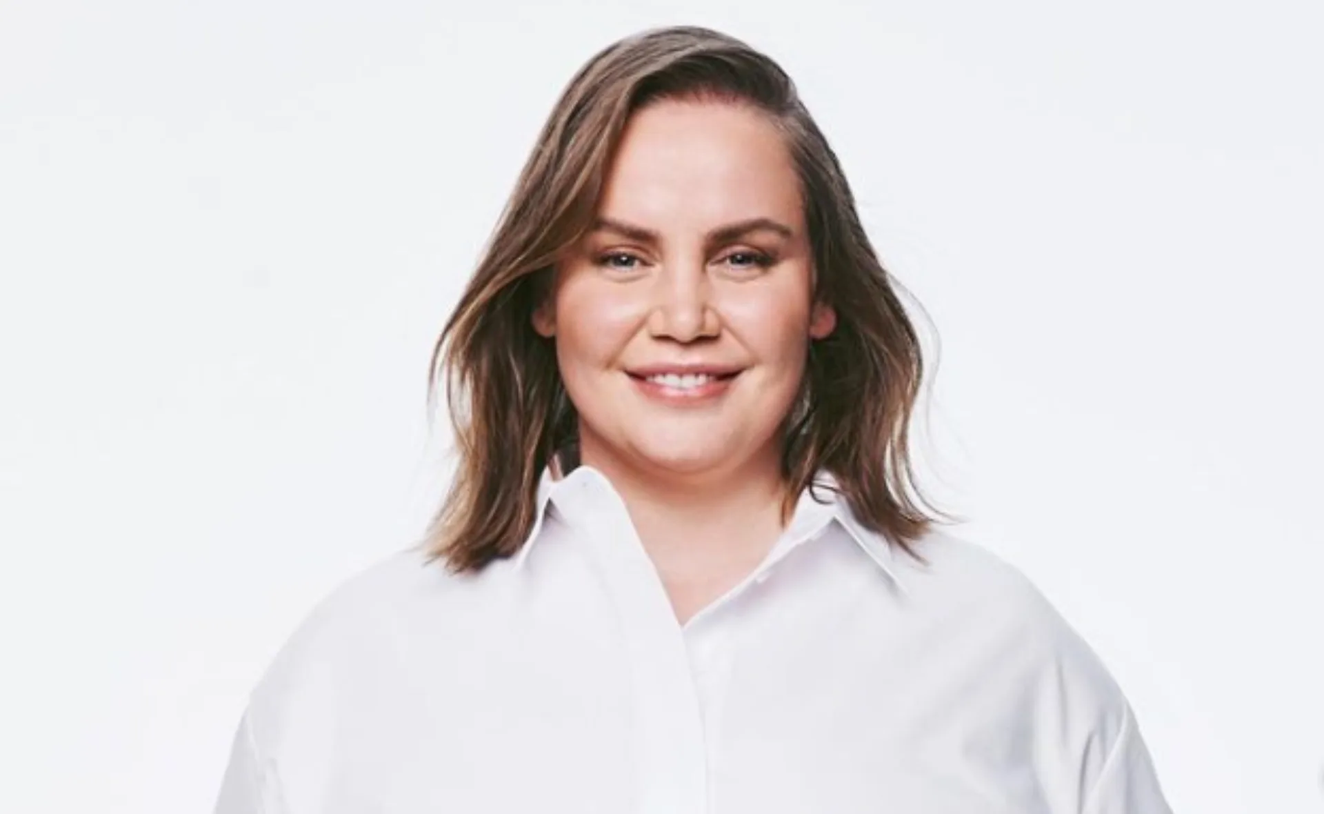 A woman smiling in a white shirt against a plain background.