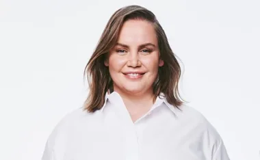 A woman smiling in a white shirt against a plain background.