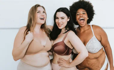 Three smiling women in different styles of bras stand together, displaying body positivity and diversity.