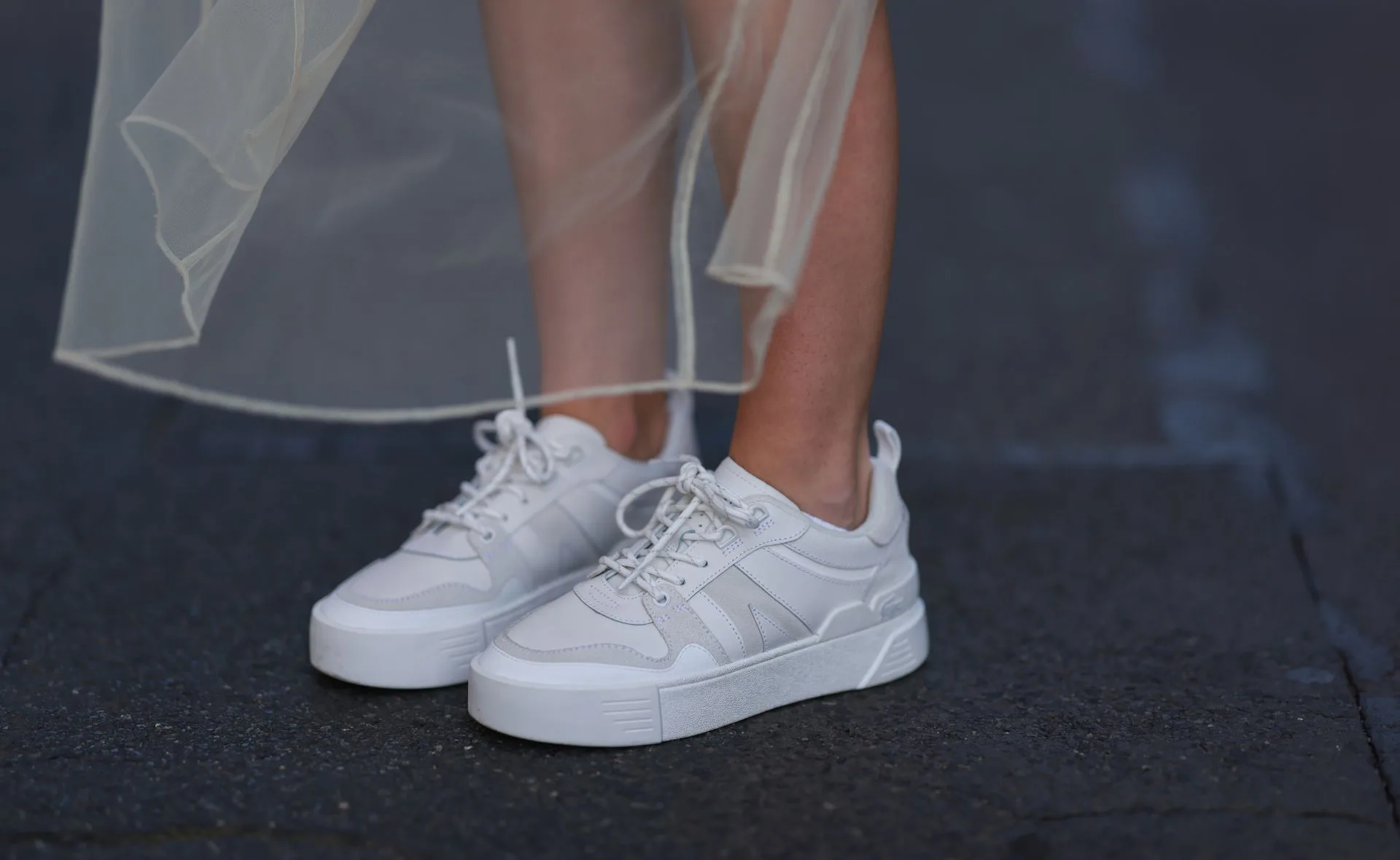White sneakers paired with a sheer skirt, worn by a person standing on a dark pavement.