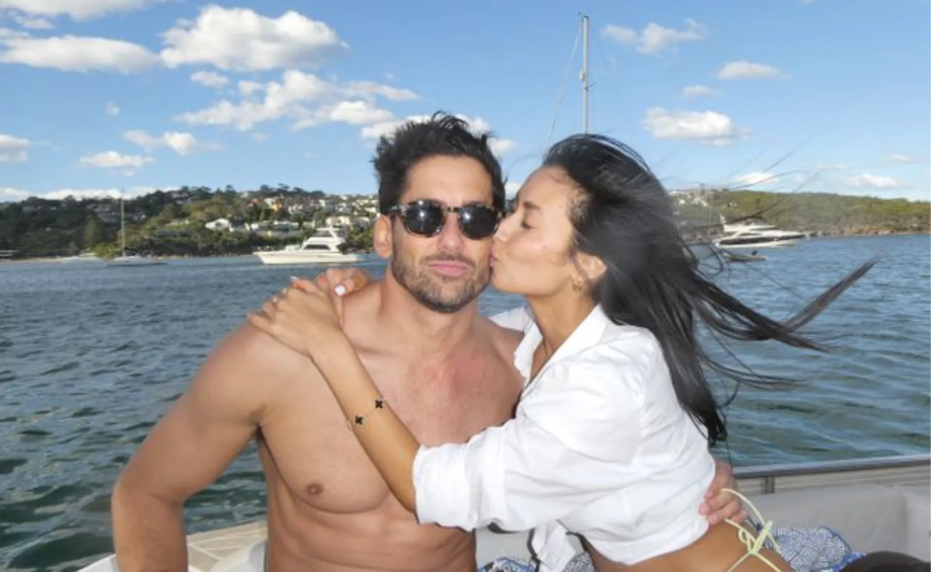 Man and woman embracing on a boat; woman kisses him on the cheek.