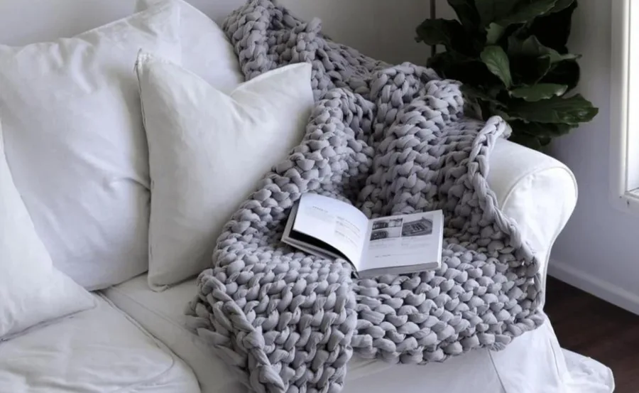 A chunky knit blanket on a white sofa with an open book on top.