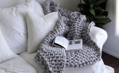 A chunky knit blanket on a white sofa with an open book on top.