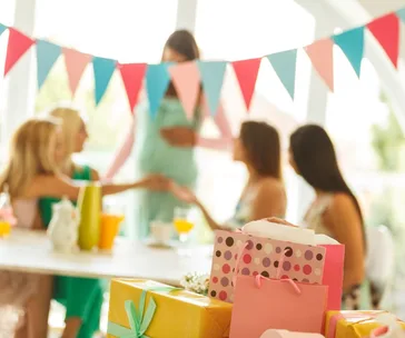 A baby shower with gifts, festive bunting, and women gathered around a table, one touching a pregnant woman's belly.
