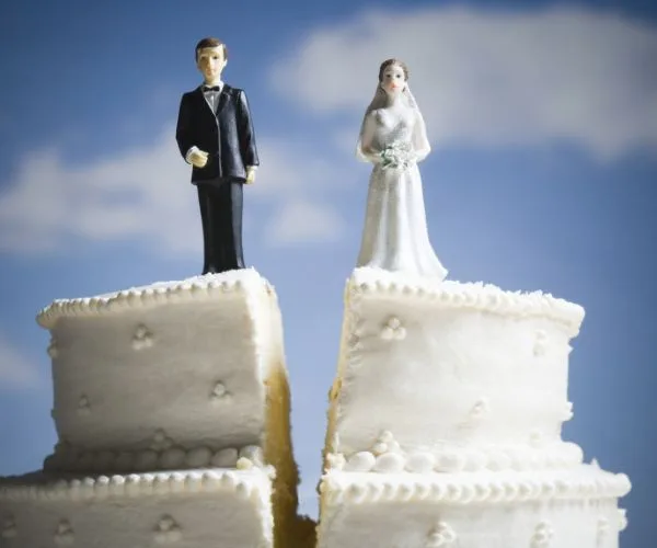 Wedding cake with split layers, topped with bride and groom figurines, symbolizing divorce or separation.