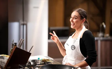 "Malissa from MasterChef Australia 2023 gestures while cooking in the kitchen, smiling and wearing a branded apron."