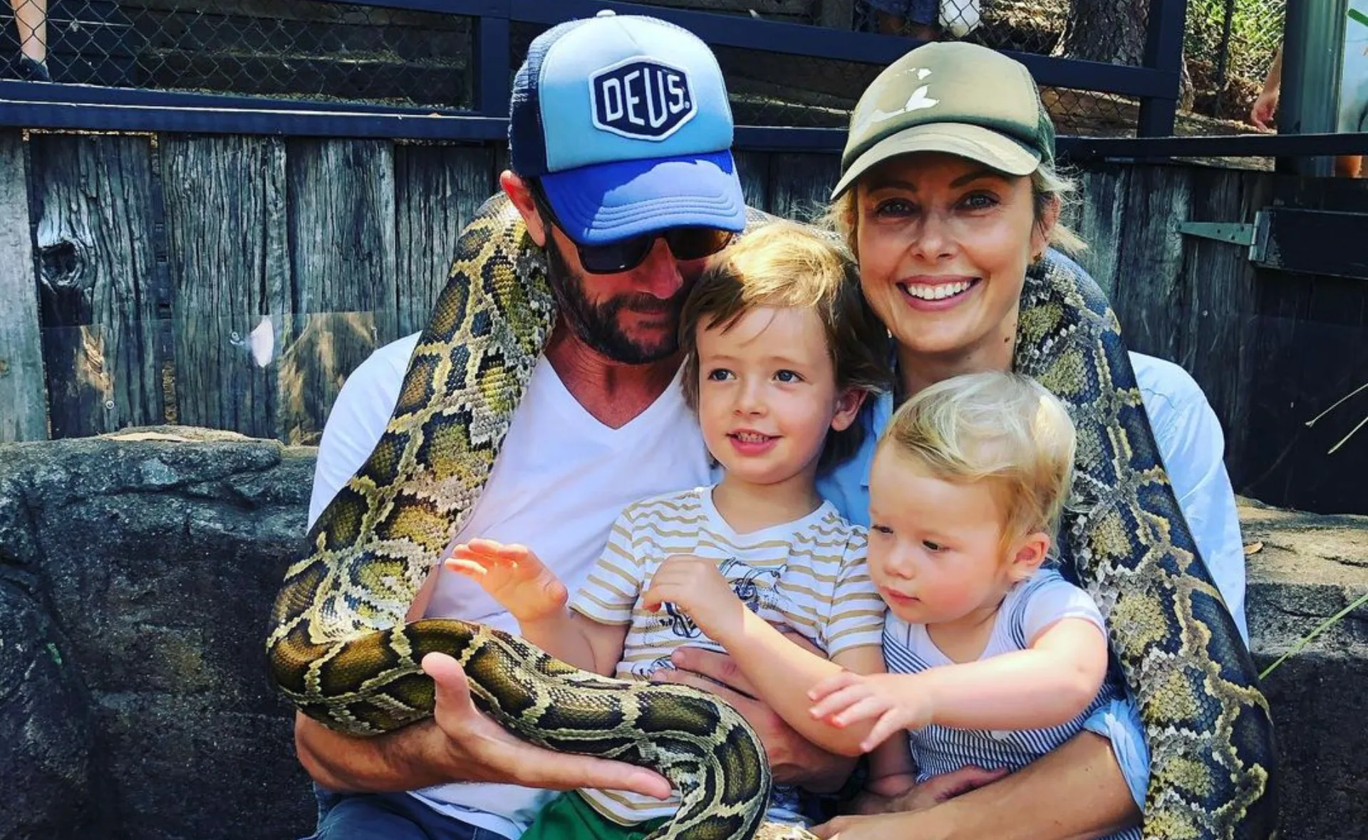 Family sitting with a large snake wrapped around them, two children in the middle, smiling adults on either side.