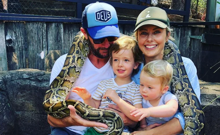 Family sitting with a large snake wrapped around them, two children in the middle, smiling adults on either side.