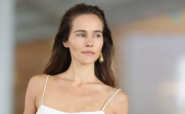A woman with long hair wearing a white spaghetti strap top, gazing to the side.