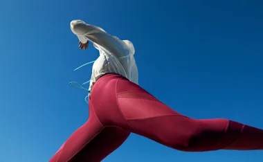 Person in maroon leggings and white jacket running under clear blue sky.