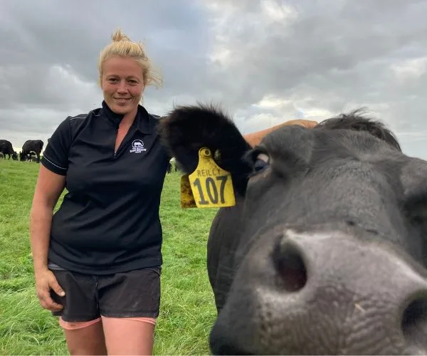 Person standing beside a cow with an ear tag numbered 107 in a grassy field.
