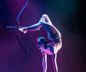 Contortionist performs a backbend, holding a bow with feet, poised to shoot an arrow.