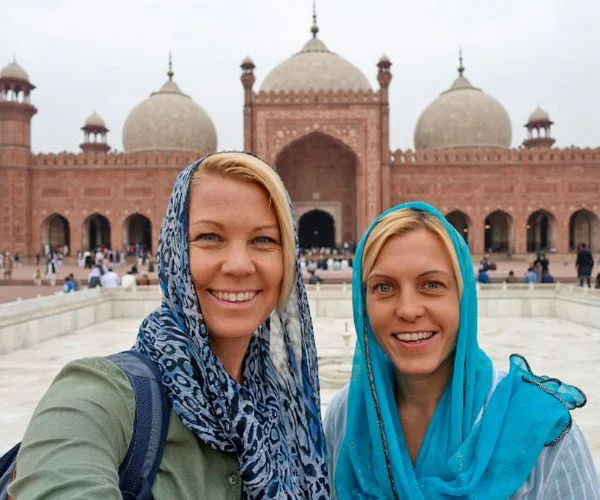 Two women with headscarves taking a selfie in front of a historic mosque with large domes in the background.