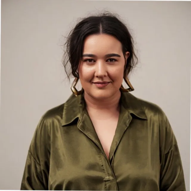 A person with dark hair in a green shirt and large earrings, smiling softly against a neutral background.