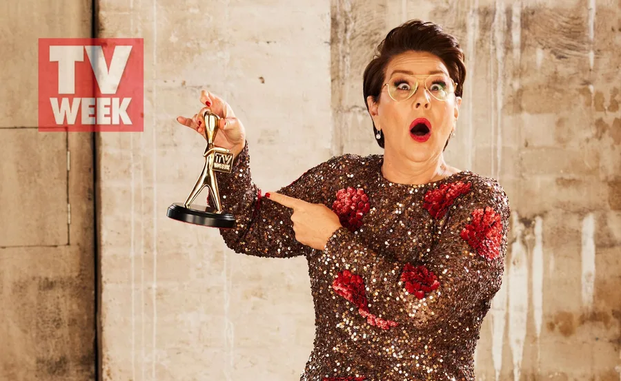 Person in sequin dress holding a TV WEEK Logie award, pointing with a surprised expression.
