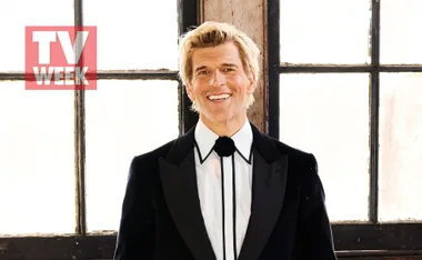 Man in tuxedo smiling in front of large windows, with a "TV Week" logo on the image.