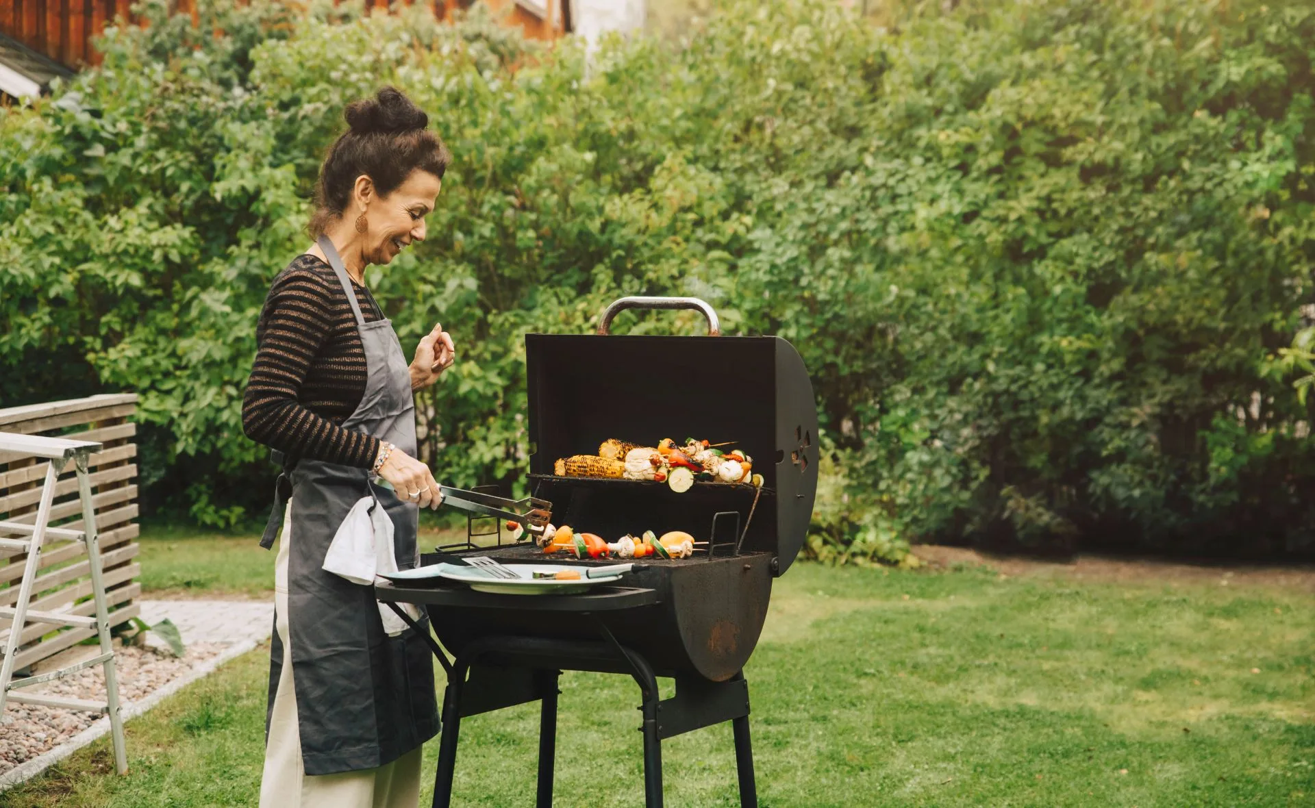 Woman grilling vegetables on a barbecue in a garden.