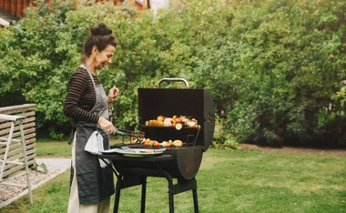 Woman grilling vegetables on a barbecue in a garden.