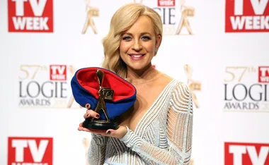 A woman in a white dress holds a TV Week Logie Award, smiling at the 57th TV Week Logie Awards event.