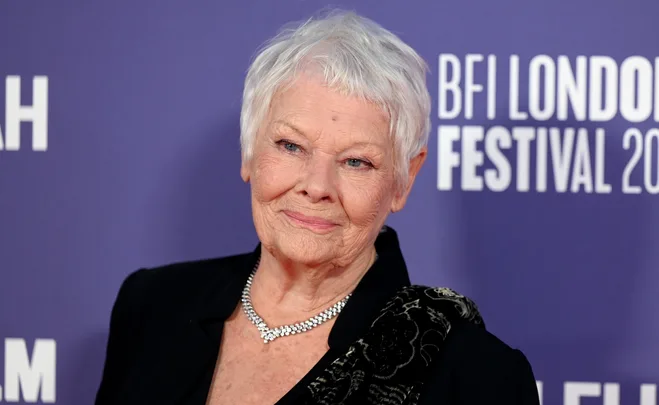 Elderly woman with a short white haircut, wearing a necklace, at a purple backdrop event.
