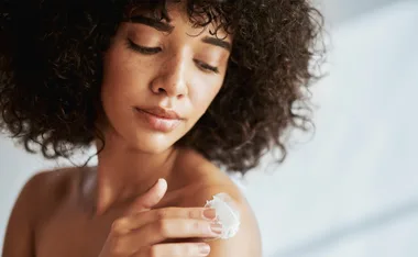Woman applying cream to her shoulder with a serene expression, highlighting a skincare routine.