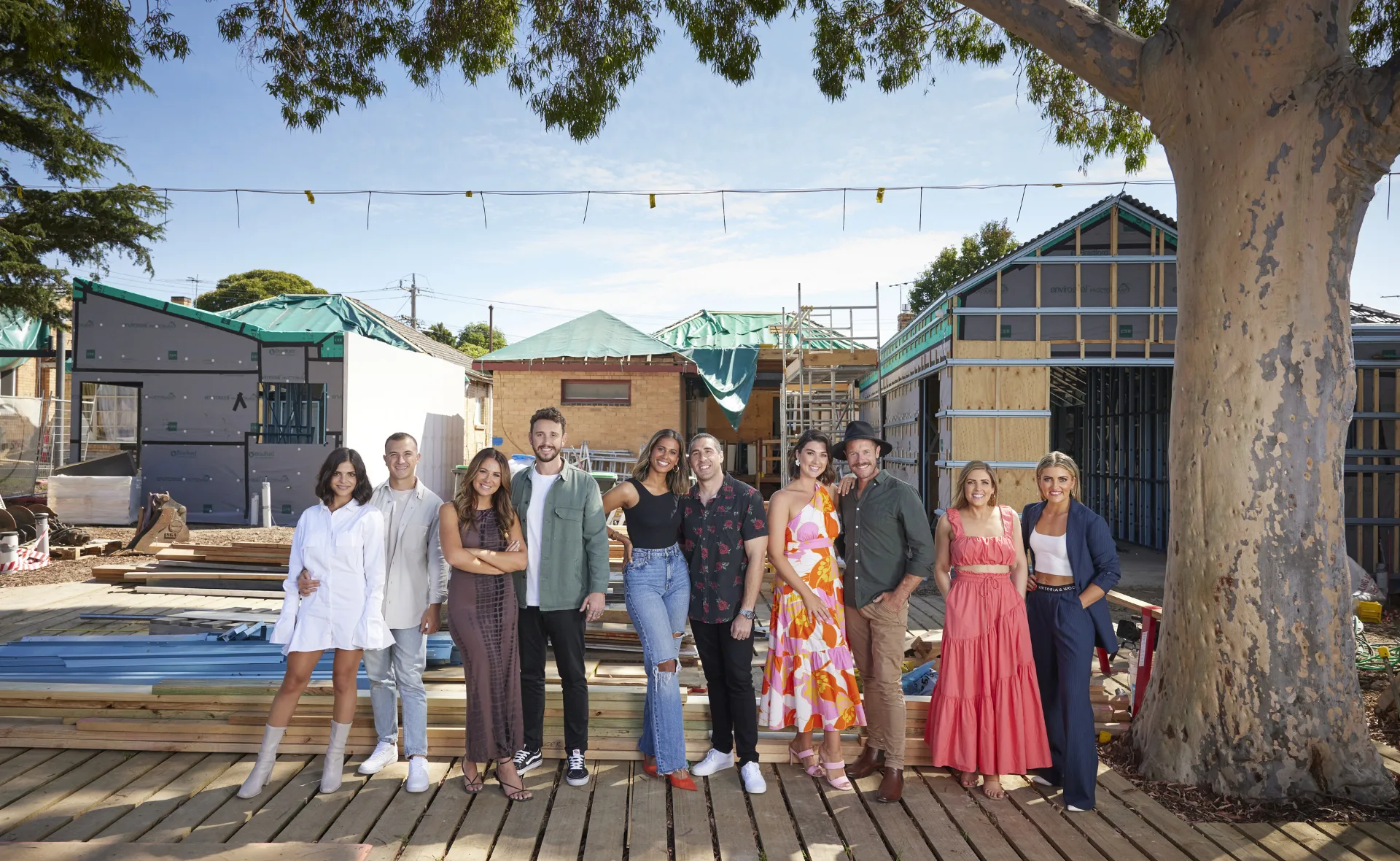 Group of people posing in front of a construction site with partially built houses, under a large tree.