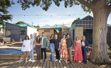 Group of people posing in front of a construction site with partially built houses, under a large tree.