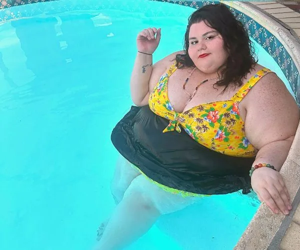 Woman in yellow floral swimsuit relaxing in a pool, with partial view of poolside tiles.