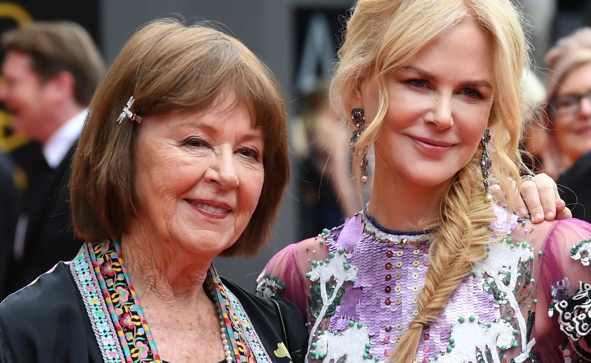 Two women smiling at an event, one wearing a purple dress, the other with short brown hair and a colorful scarf.