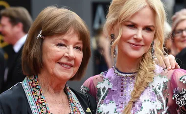 Two women smiling at an event, one wearing a purple dress, the other with short brown hair and a colorful scarf.