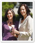 Two women standing together outdoors, smiling, with one holding a white rose.